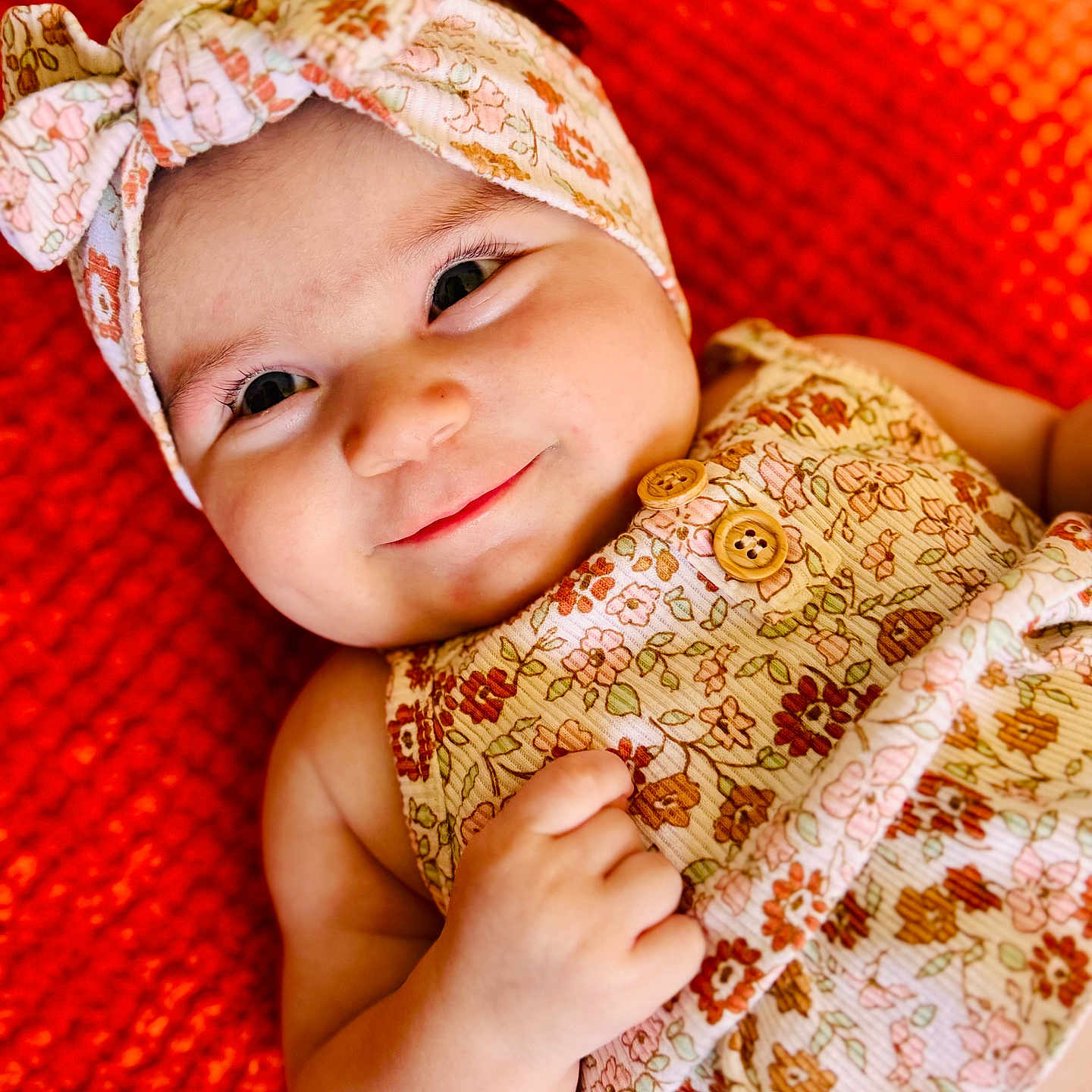 Morgana is registered to the contest to win money with this photo: baby, child, closeup, cute, dress, floral_pattern, hand, happy, headband, indoors, infant, lying_down, orange_background, person, portrait, skin, smile, soft_lighting, texture, young