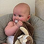 baby, infant, pacifier, plush_toy, blanket, diaper, cushion, seated, indoor, cute, child, soft_texture, neutral_colors, comfort, curious, skin, head, hand, face, expression