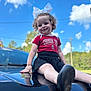 Delilah is registered to the contest to win money with this photo: toddler, child, curly_hair, white_bow, red_shirt, black_skirt, black_car, car_hood, outdoor, blue_sky, clouds, smiling, sitting, daylight, casual_clothing, reflection, nature, trees, portrait, happy