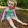 toddler, child, curly_hair, blue_eyes, smiling, water, creek, rocks, outdoor, nature, sunlight, greenery, swimsuit, floral_pattern, playful, sitting, happy, summer, skin, barefoot