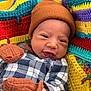 baby, infant, smile, hat, mittens, blanket, crochet, colorful, plaid_clothing, cozy, warm, face, handwear, cute, portrait, indoors, happy, child, newborn, fabric
