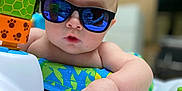 Elliot is registered to the contest to win money with this photo: baby, sunglasses, reflection, toy, activity_center, child, infant, hand, face, outdoor, greenery, colorful, playtime, summer, cute, portrait, closeup, expression, skin, casual