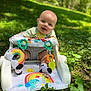 baby, walker, outdoor, grass, greenery, toy, rainbow, leaf_toy, socks, smiling, happy, sunlight, nature, child, infant, cute, playful, seat, colorful, daylight