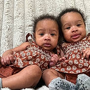 Nevaeh is registered to the contest to win money with this photo: baby, twins, infant, child, dress, brown, pattern, sock, lying_down, blanket, cute, portrait, two_people, face, skin, hand, foot, smile, indoors, person