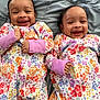 Nevaeh is registered to the contest to win money with this photo: baby, smiling, twin, floral_pajamas, lying_down, blanket, cute, infant, happy, face, child, sleepwear, matching_outfits, two, person, indoors, head, skin, expression, joy