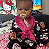 baby, bed, bedroom, black, child, face, fluffy, hello_kitty, home, indoor, infant, pacifier, patterned_blanket, person, pink, portrait, robe, sitting, smiling, television