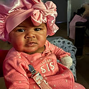 Kemani is registered to the contest to win money with this photo: baby, child, pink, headwear, bow, indoor, clothing, face, person, infant, cute, young, portrait, sitting, fabric, room, expression, closeup, soft_lighting, accessory