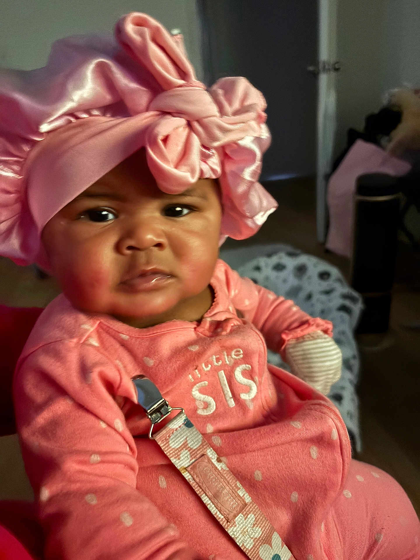 Kemani is registered to the contest to win money with this photo: baby, child, pink, headwear, bow, indoor, clothing, face, person, infant, cute, young, portrait, sitting, fabric, room, expression, closeup, soft_lighting, accessory