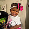Kemani joined the competition — help win amazing prizes! adult, baby, child, door, dress, hair_bow, headband, home, indoors, pacifier, photography, pink_clothing, polka_dot, portrait, skirt, smiling, superhero_shirt, toddler, wall, white_shirt