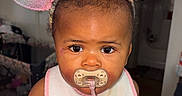 Kemani is registered to the contest to win money with this photo: baby, bib, bow, child, close_up, clothing, colorful, dark_hair, eyes, face, glitter, headband, home, indoor, infant, mouse_ears, pacifier, portrait, sitting, smiling