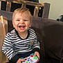Tiago a rejoint le concours — aidez-le/la à gagner de superbes lots ! toddler, child, smiling, toy, remote_control, striped_sweater, couch, sitting, happy, indoor, yellow_ball, purple_socks, wooden_chair, blue_banner, face, person, furniture, play, young_child, casual_clothing