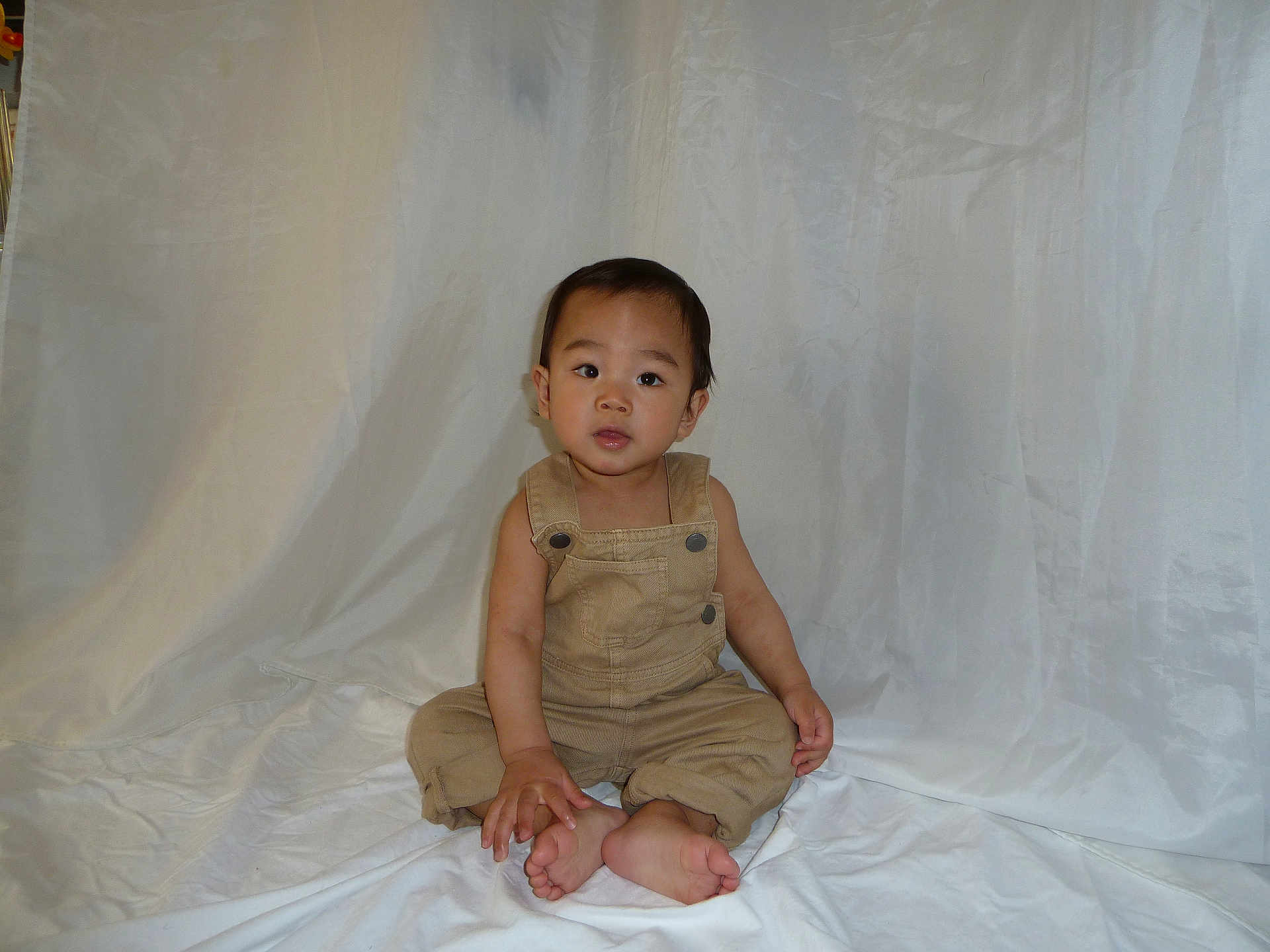 Isaiah joined the competition — help win amazing prizes! toddler, child, baby, overalls, barefoot, sitting, curious, studio, fabric, white_backdrop, portrait, young, innocent, clothing, person, indoor, cute, expression, baby_face, hands