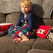 Atlas joined the competition — help win amazing prizes! child, pajamas, christmas_theme, sitting, couch, pillow, blanket, indoor, foot, clothing, person, expression, holiday, living_room, home, furniture, cozy, blond_hair, casual, relaxed