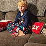 blanket, blond_hair, casual, child, christmas_theme, clothing, couch, cozy, expression, foot, furniture, holiday, home, indoor, living_room, pajamas, person, pillow, relaxed, sitting