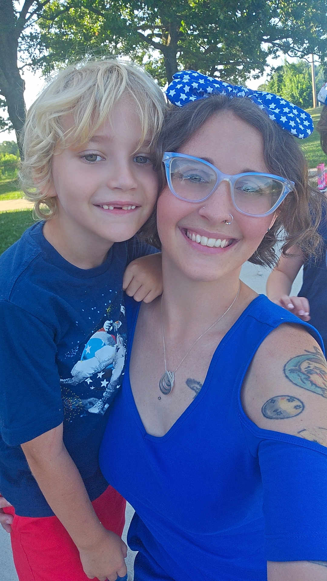 Atlas joined the competition — help win amazing prizes! child, woman, glasses, blue_dress, tattoo, smile, outdoor, trees, sunlight, happy, hug, short_hair, blonde_hair, accessories, park, casual_clothing, nature, portrait, family, daylight