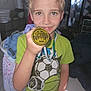 Atlas is registered to the contest to win money with this photo: child, boy, medal, green_tshirt, sports, indoor, laundry, clutter, smile, face, hand, short_hair, floor_tiles, clothing, person, trophy, award, flash, proud, young