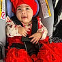 Rosie Mendieta joined the competition — help win amazing prizes! baby, infant, child, car_seat, red_hat, bow, red_dress, harness, smiling, hands, bracelet, face, portrait, tulle, floral_print, gray_upholstery, safety_label, closeup, cozy, newborn