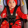 baby, infant, car_seat, red_hat, pom_poms, holiday_pajamas, seat_harness, closeup, portrait, blue_eyes, cute, festive, socks, hands, lips, soft_padding, winter_clothing, warning_label, straps, sitting