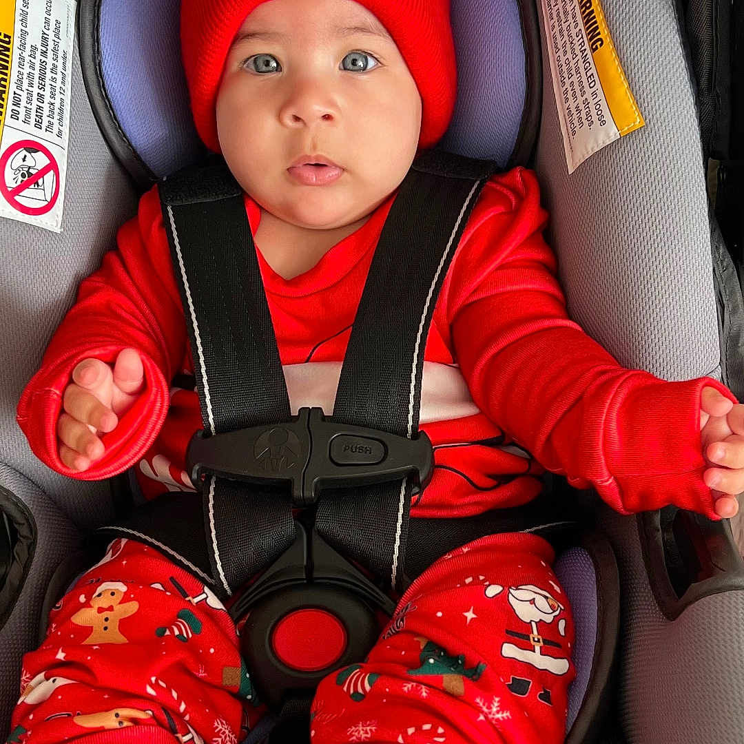 Rosie Mendieta is registered to the contest to win money with this photo: baby, blue_eyes, car_seat, closeup, cute, festive, hands, holiday_pajamas, infant, lips, pom_poms, portrait, red_hat, seat_harness, sitting, socks, soft_padding, straps, warning_label, winter_clothing