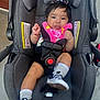 baby, car_seat, evenflo, smiling, pink_bib, black_hair, bracelet, socks, shoes, checkered_shoes, safety_harness, infant, cute, tongue_out, child, seatbelt, gray_fabric, outdoor, concrete_floor, person