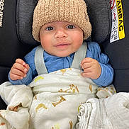 Kamari is registered to the contest to win money with this photo: baby, child, car_seat, hat, knit_hat, blanket, giraffe_print, blue_clothing, infant, cute, smiling, face, hands, child_seat, safety_harness, indoor, soft_texture, warm_clothing, newborn, person