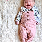 Cassie a rejoint le concours — aidez-le/la à gagner de superbes lots ! baby, infant, smiling, pink_overalls, floral_shirt, blanket, embroidery, name, cassie, happy, lying_down, cute, child, portrait, clothing, feet, hands, face, indoors, soft_light
