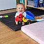 baby, child, toy, dump_truck, smile, happy, indoor, play_mat, floor, cushion, wooden_floor, shelf, storage, container, plastic_toy, person, infant, cute, home, playtime