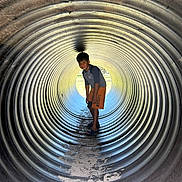 Christian is registered to the contest to win money with this photo: child, boy, tunnel, metal, outdoor, playground, adventure, light, shadow, curious, smiling, shorts, sand, texture, cylindrical, young, standing, casual, fun, daylight