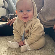 Zachary is registered to the contest to win money with this photo: baby, child, hoodie, carpet, smile, indoor, person, dog, couch, plant, window, sitting, happy, cozy, floor, hand, casual_clothing, home, relaxed, portrait