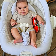Enzo is registered to the contest to win money with this photo: baby, infant, child, smiling, rocker, baby_toy, cushion, clothing, shorts, shirt, floor, tile_floor, home_interior, seat_belt, baby_seat, foot, hand, face, person, indoor