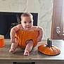 Enzo is registered to the contest to win money with this photo: baby, pumpkin, table, indoor, child, cute, smiling, autumn, hollowed_pumpkin, face, legs, arms, wooden_table, orange, cozy, fireplace, natural_light, festive, curious, person