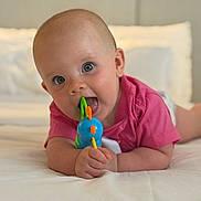 Flavie participe au concours pour gagner de l'argent avec cette photo : baby, bed, blue_toy, child, cute, expression, face, hand, happy, head, indoors, infant, mouth, person, pink_shirt, playing, skin, tongue, toy, young