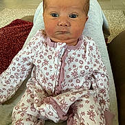 Lainey is registered to the contest to win money with this photo: baby, child, infant, onesie, floral_pattern, person, face, eyes, expression, sitting, lap, home, carpet, furniture, wood_floor, blanket, cozy, cute, indoors, portrait