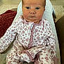 baby, child, infant, onesie, floral_pattern, person, face, eyes, expression, sitting, lap, home, carpet, furniture, wood_floor, blanket, cozy, cute, indoors, portrait