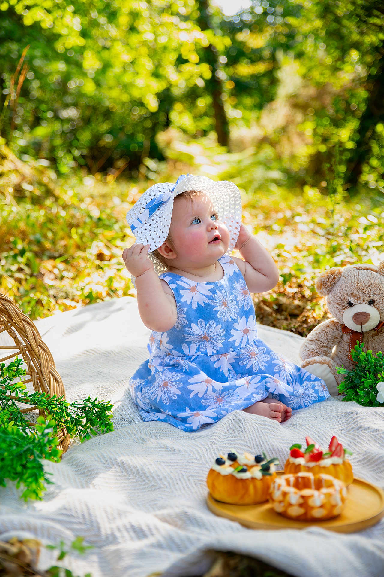 Shelby participe au concours pour gagner de l'argent avec cette photo : baby, child, blue_dress, sunhat, outdoor, picnic, blanket, teddy_bear, pastries, greenery, nature, cute, sitting, curious, summer, food, plate, flower_pattern, daylight, happy