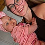 baby, blue_eyes, bow, casual, child, closeup, face, family, glasses, happy, headwear, holding, indoor, light_skin, person, pink_clothing, portrait, smile, tattoo, woman