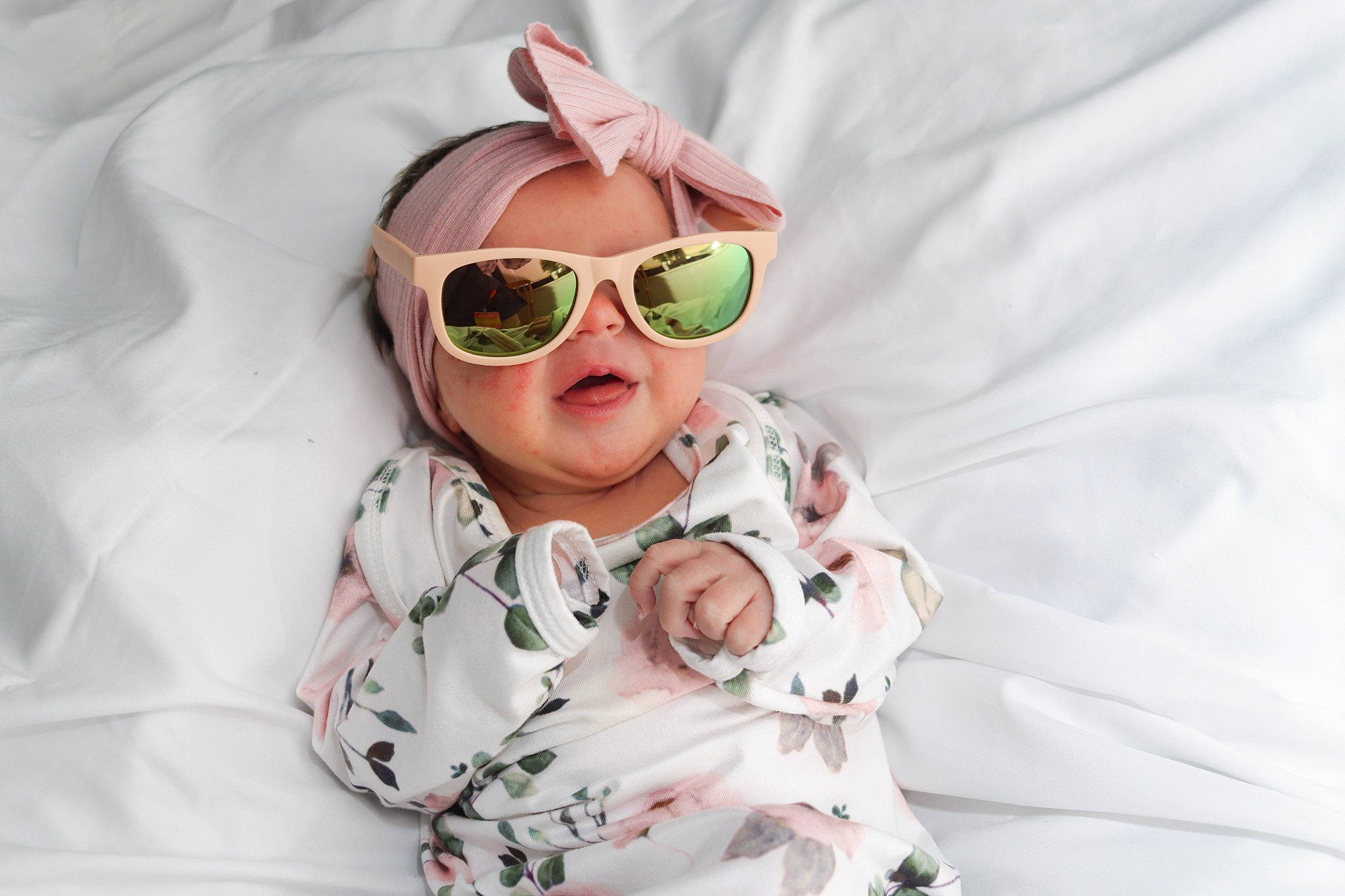 Lainey is registered to the contest to win money with this photo: baby, baby_toddler_clothing, comfort, eye, eyewear, fun, glasses, goggles, happy, headwear, linens, mouth, person, personal_protective_equipment, petal, pink, sleeve, smile, sunglasses, textile