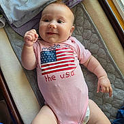 Charli joined the competition — help win amazing prizes! baby, infant, smiling, onesie, american_flag, pink_clothing, lying_down, blanket, diaper, indoors, window, soft_fabric, cute, happy, child, person, skin, face, chubby_arms, natural_light