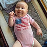 baby, infant, smiling, onesie, american_flag, pink_clothing, lying_down, blanket, diaper, indoors, window, soft_fabric, cute, happy, child, person, skin, face, chubby_arms, natural_light
