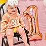 baby, toddler, child, bow_headband, white_bow, knitted_sweater, flower_detail, wooden_chair, rose_gold_balloon, number_one_balloon, pink_backdrop, birthday_party, celebration, smiling, sitting, legs, bare_feet, portrait, cute, party_decor