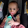 Jessie joined the competition — help win amazing prizes! baby, pacifier, bottle, car_seat, blanket, infant, child, blue_eyes, pink, holding, seated, indoors, warning_label, clothing, cute, portrait, small_hands, looking_at_camera, young_child, baby_girl