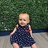 baby, child, polka_dot_dress, blue_dress, red_bow, smiling, sitting, floor, wooden_floor, greenery, leaves, background, indoors, infant, cute, portrait, happy, person, face, eyes