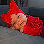 Kyra-Mae is registered to the contest to win money with this photo: baby, infant, red_bow, red_clothing, soft_surface, gray_couch, window, curtains, indoors, portrait, cute, cozy, headwear, closeup, child, smiling, resting, natural_light, home, person