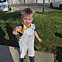 Kenzo a rejoint le concours — aidez-le/la à gagner de superbes lots ! child, toddler, boy, pointing, smiling, blond_hair, overalls, sandals, grass, concrete, parking_lot, cars, pole, shadow, building, sunny, outdoor, emotions, portrait, casual_clothing