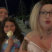 Cora is registered to the contest to win money with this photo: casual, clothing, cone, face, friends, glasses, hair, hairstyle, ice_cream, lipstick, night, outdoor, park, people, person, selfie, smiling, street_light, table, tattoo