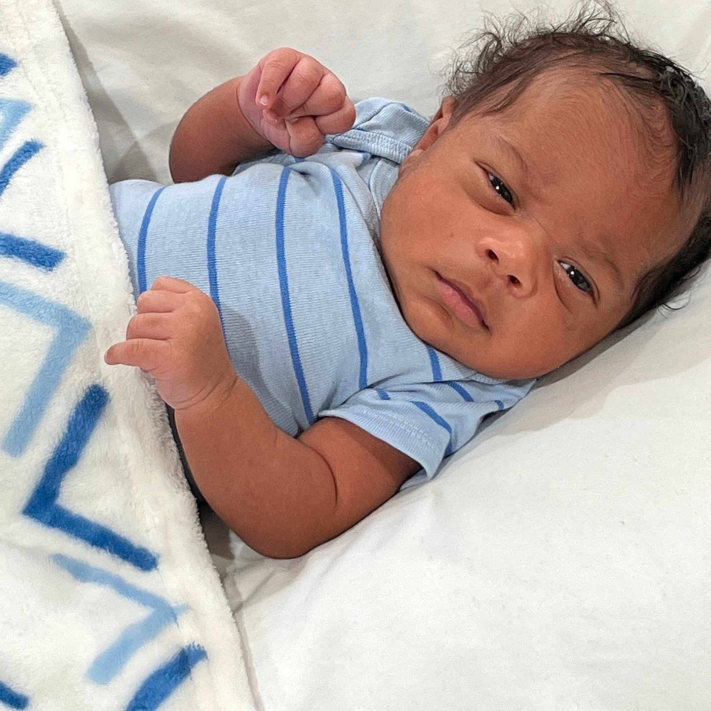 Marshawn joined the competition — help win amazing prizes! baby, blanket, blue_stripes, clothing, cute, face, fist, hair, indoor, infant, laying_down, looking, newborn, person, portrait, skin, soft_surface, toddler, white_blanket, young_child