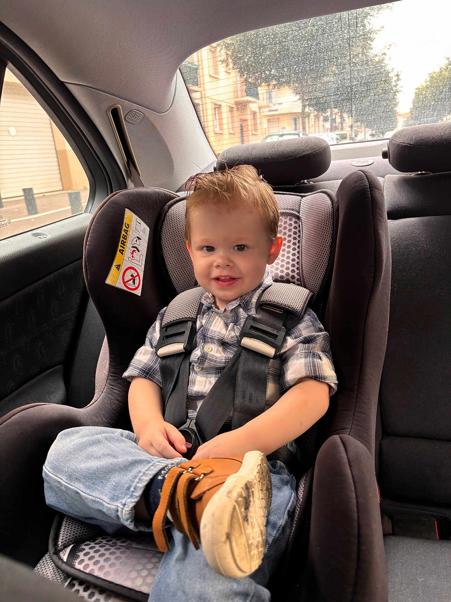Tobias participe au concours pour gagner de l'argent avec cette photo : toddler, child, car_seat, car_interior, seat_belt, smile, happy, hair, jeans, boot, window, rain, urban, street, daylight, safety, plaid_shirt, seat, vehicle, casual_clothing