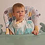 toddler, child, high_chair, bib, face, expression, indoor, furniture, table, clothing, person, young_child, curious, sitting, smiling, skin, hair, hand, foot, floor