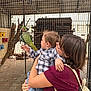 Tobias a rejoint le concours — aidez-le/la à gagner de superbes lots ! child, adult, parrot, bird, aviary, cage, wire_mesh, curiosity, interaction, animal, pet, enclosure, outdoor, person, holding, glasses, backpack, plaid_shirt, jeans, nature