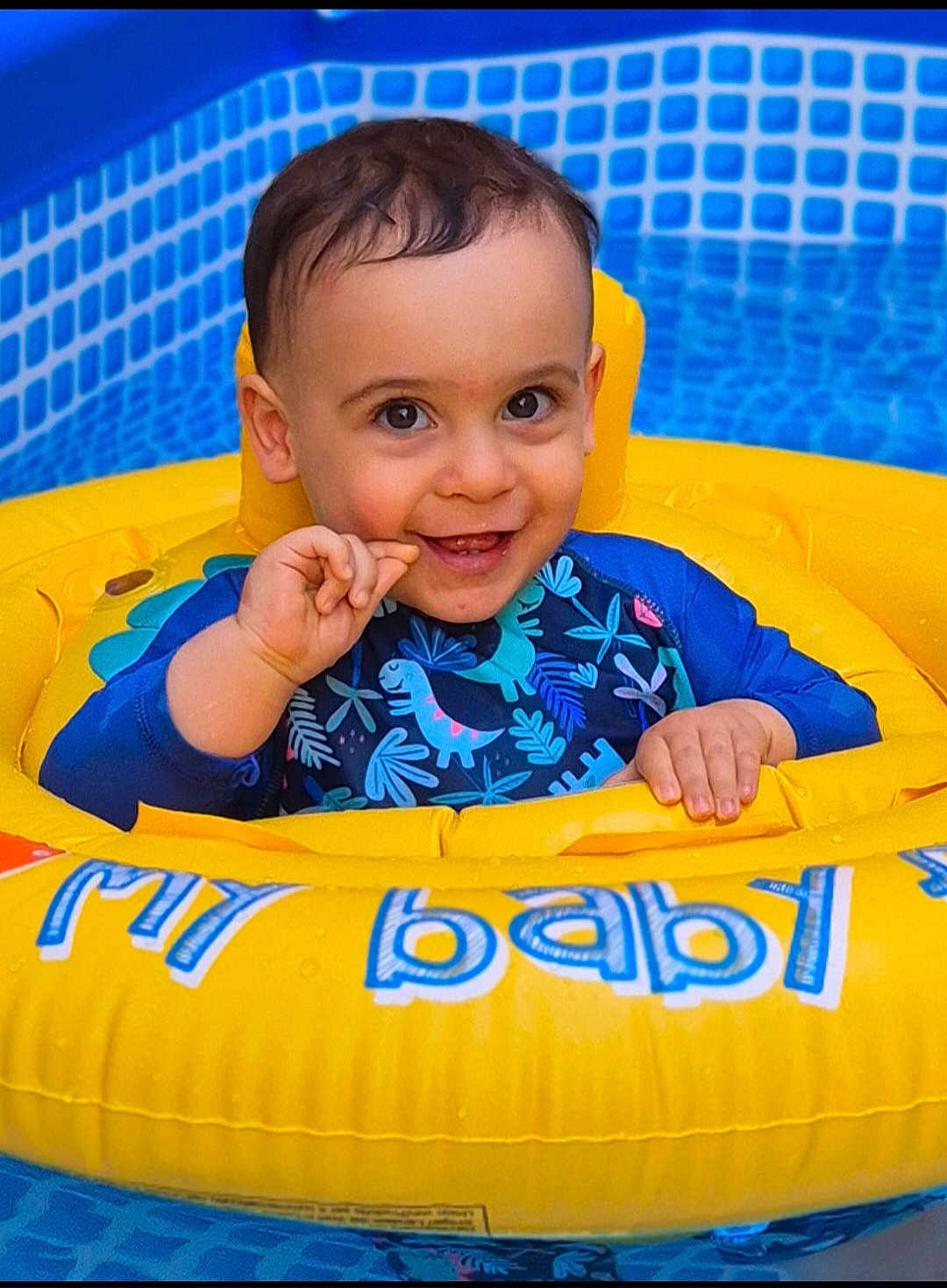 Amir a rejoint le concours — aidez-le/la à gagner de superbes lots ! baby, child, swimming_pool, inflatable_ring, yellow, blue, smiling, happy, water, splash, cute, dinosaur_pattern, swimsuit, summer, fun, outdoor, playful, young_child, floating, portrait